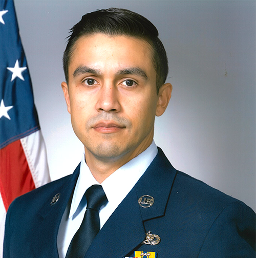 Soldier standing in uniform in front of flag.